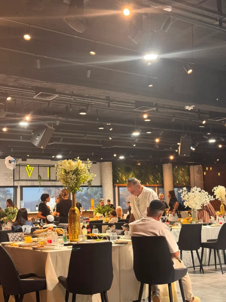 שולחנות ערוכים עם בקבוקי זהב ופרחים לבנים באירוע באולם Vine