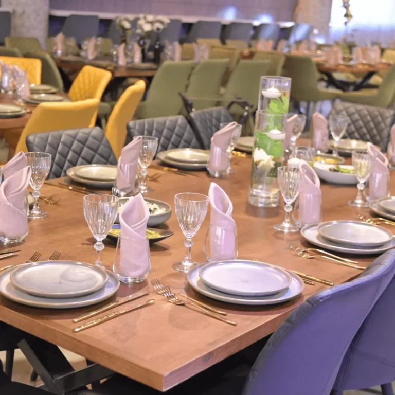 שולחן עץ ערוך עם צלחות קרמיקה, מפיות ורודות וכוסות קריסטל